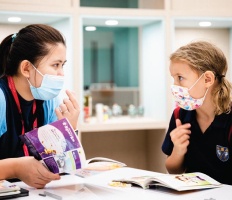 Teacher and girl reading with masks