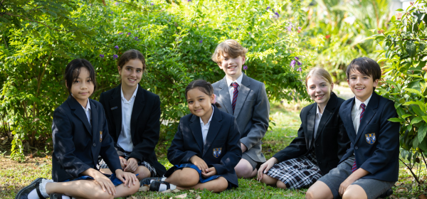 A group of Brighton College Singapore pupils in school uniform smiling together outdoors on the green campus